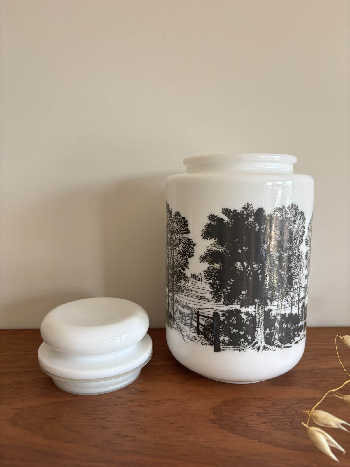 A opaline milk glass storage jar with a black transferware countryside scene.