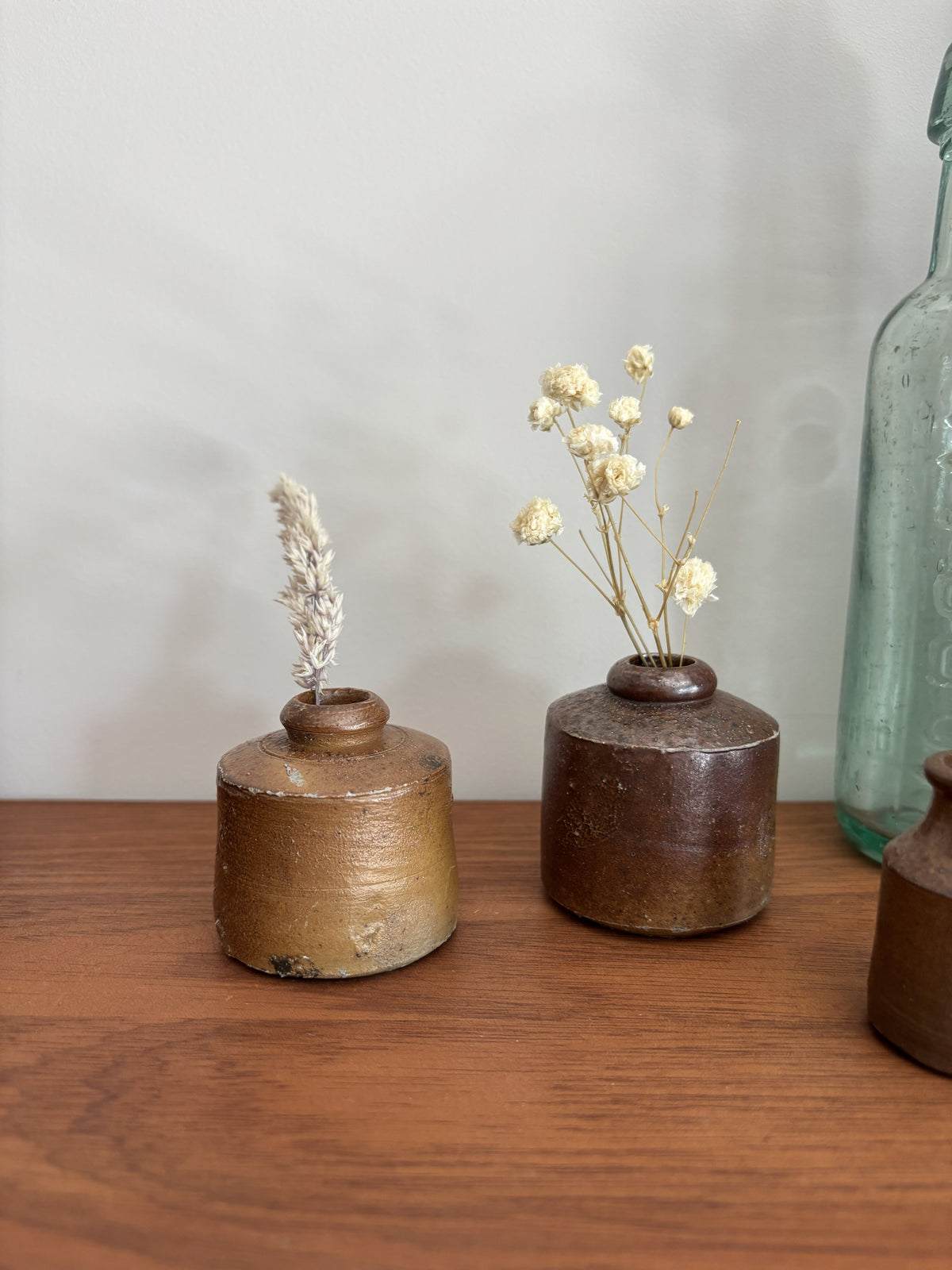 Two small vintage stoneware ink pots styled with dried flowers on a wooden tabletop against a neutral background.