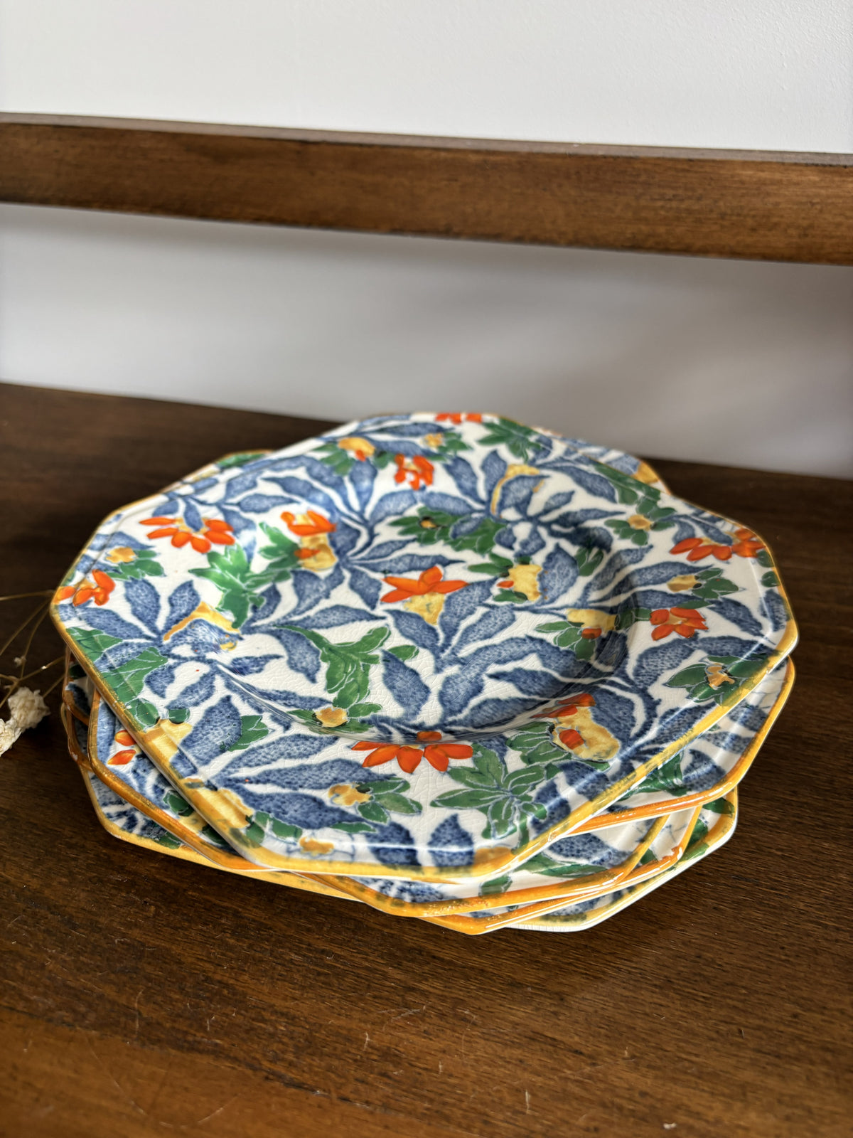 A stack of octagonal ceramic plates with a blue, green, orange, and yellow floral pattern on a white background, resting on a dark wooden table.