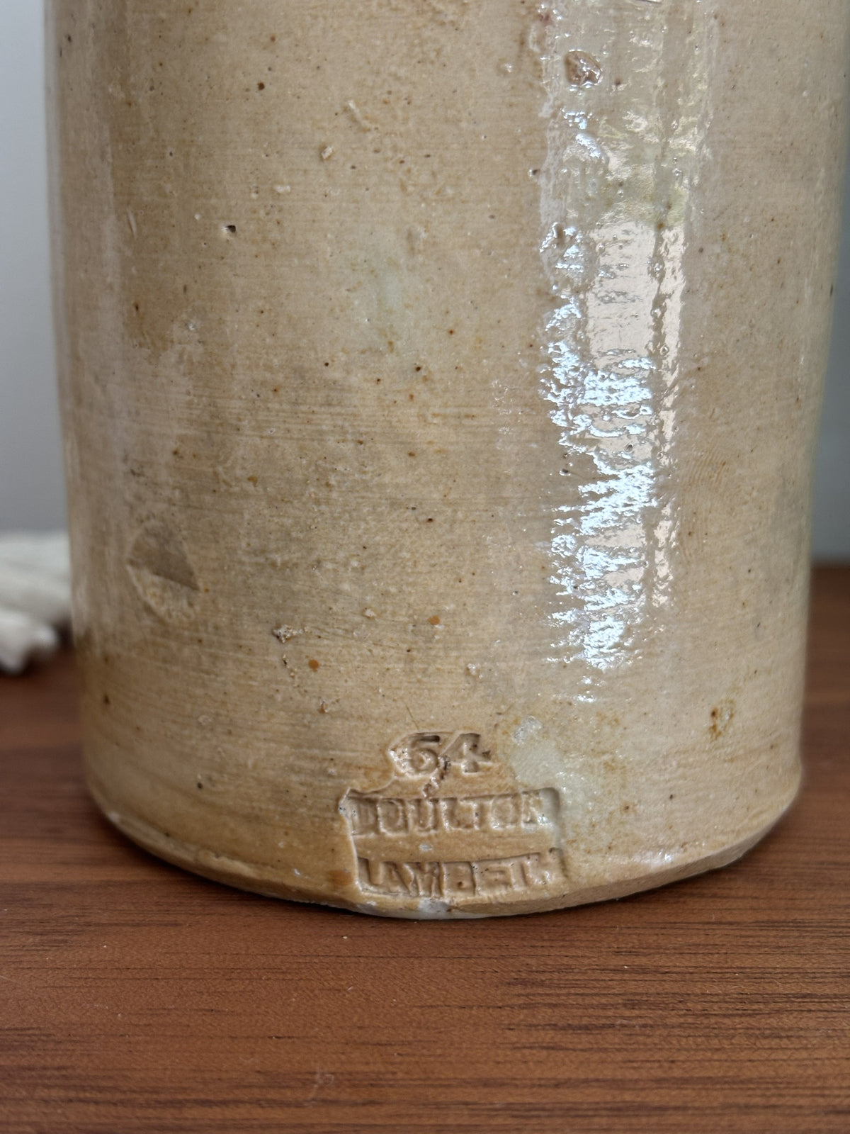 Close-up of the base of a vintage stoneware bottle, showing a stamped 'Doulton Lambeth' mark and the number '54' on a wooden surface.