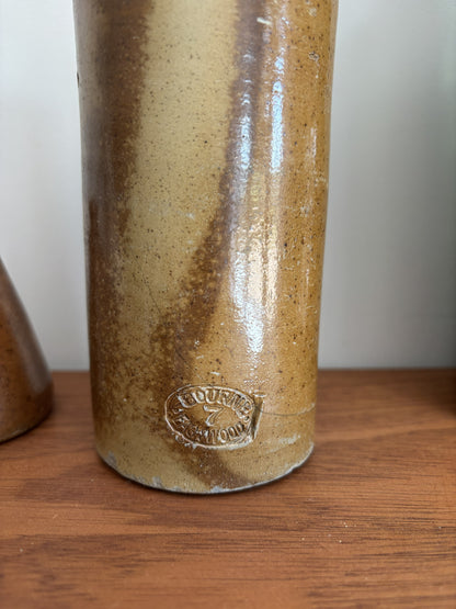 A close-up of a vintage stoneware bottle with a brown and beige marbled glaze, featuring an embossed makers mark near the base, sitting on a wooden surface.