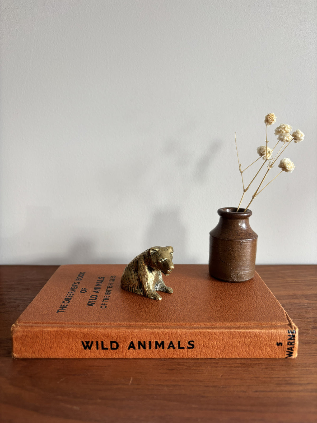 A small brass bear figurine sat on top of a brown book titled Wild Animals. 
