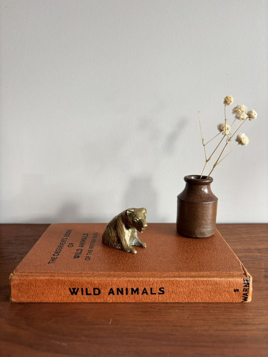 A small brass bear figurine sat on top of a brown book titled Wild Animals. 