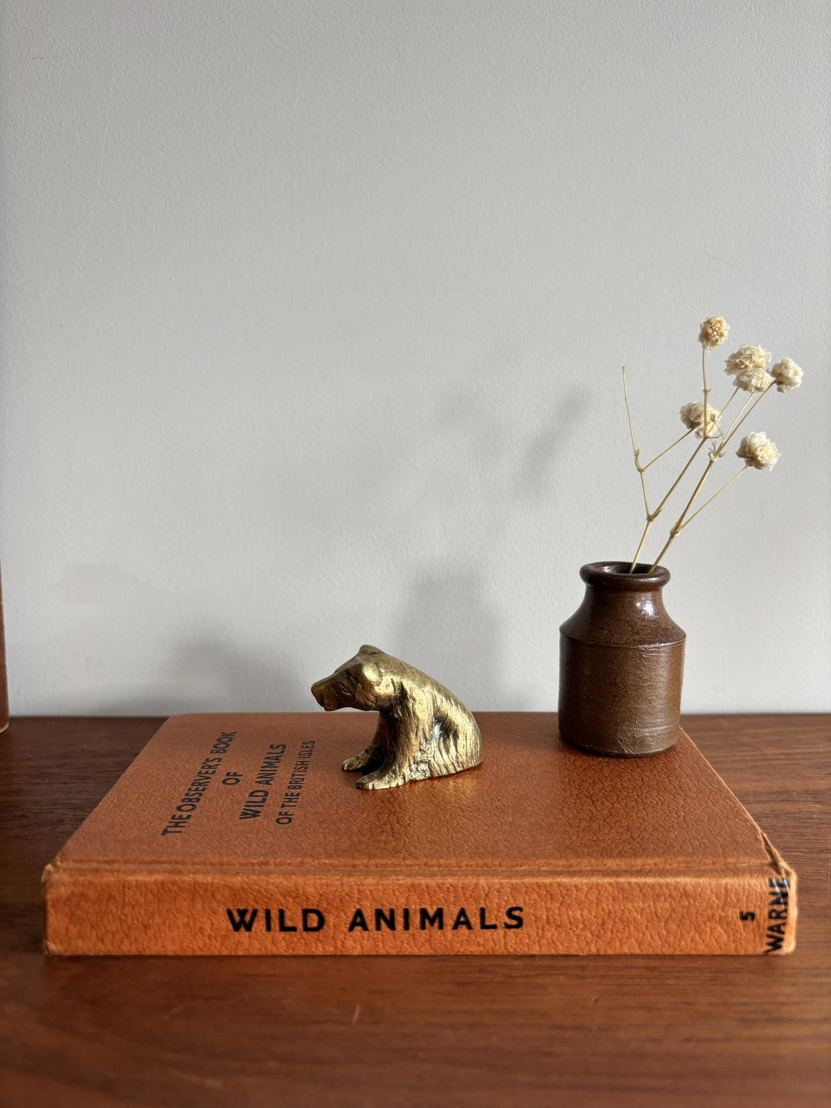 A small brass bear figurine sat on top of a brown book titled Wild Animals. 