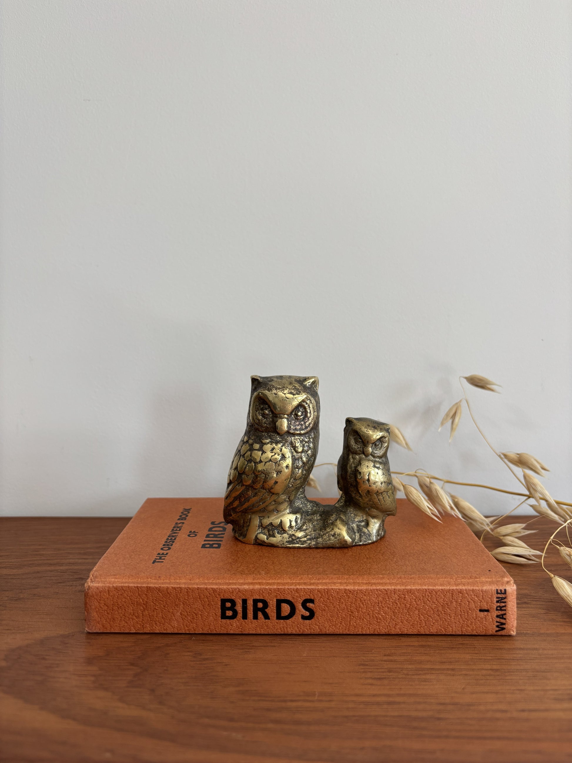 An owl and owlet figurine in a distressed metallic gold and bronze finish, displayed on top of a vintage orange book on a wooden table.
