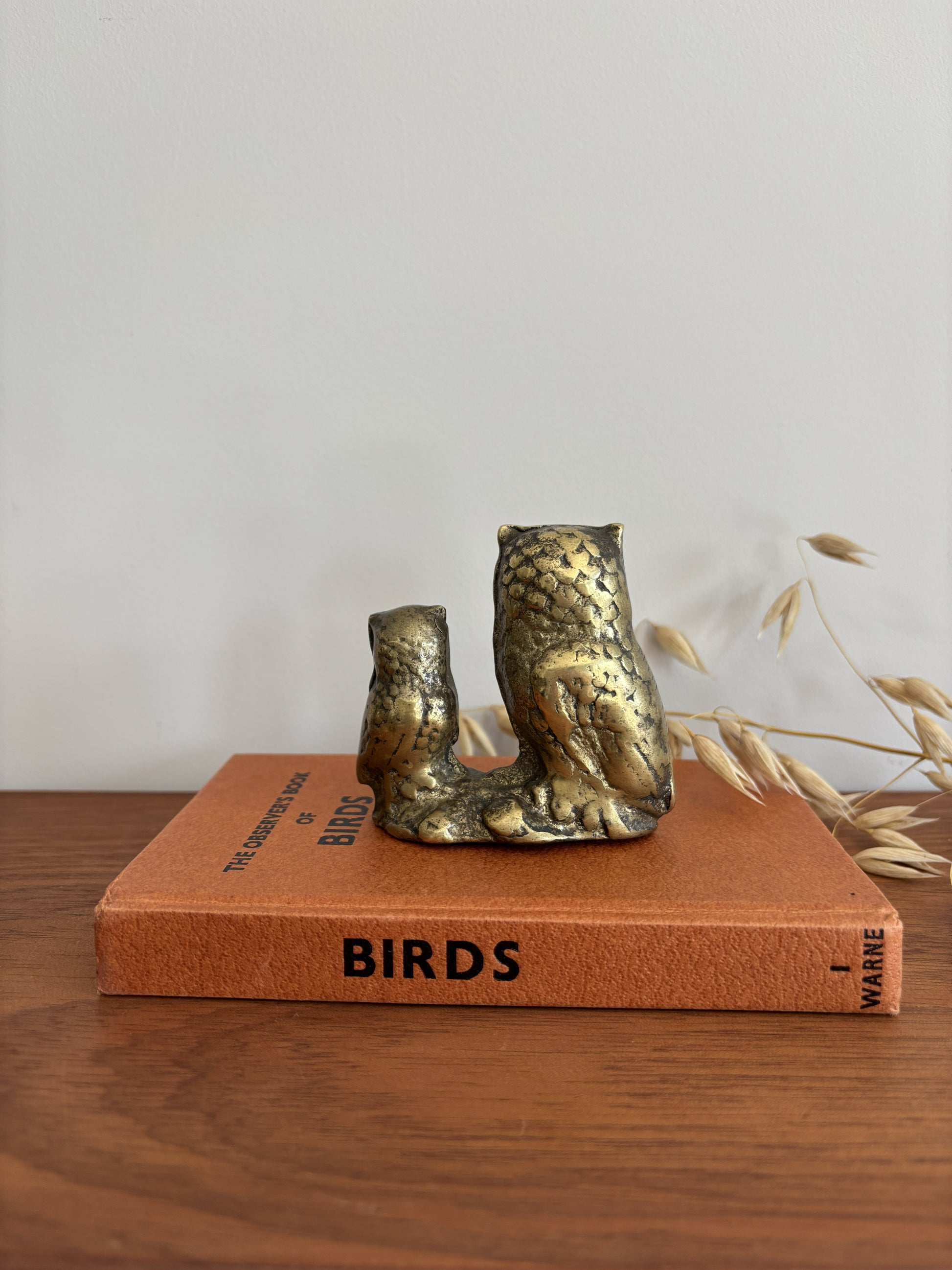 The back of an owl and owlet figurine in a distressed metallic gold and bronze finish, displayed on top of a vintage orange book on a wooden table.