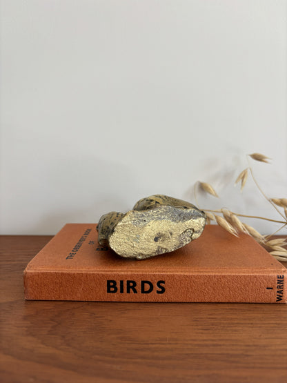 The base of an owl and owlet figurine in a distressed metallic gold and bronze finish, displayed on top of a vintage orange book on a wooden table.