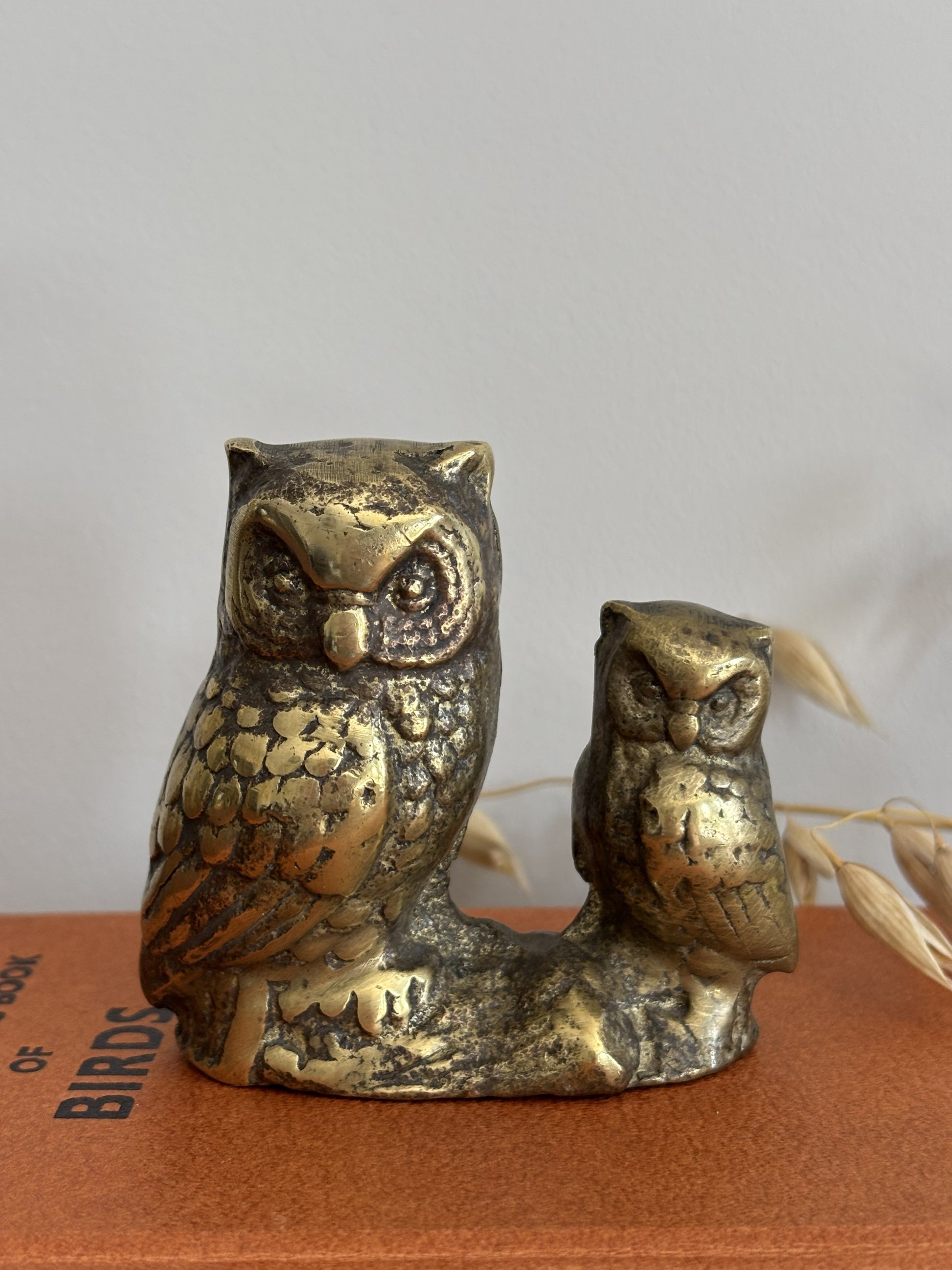 An owl and owlet figurine in a distressed metallic gold and bronze finish, displayed on top of a vintage orange book on a wooden table.