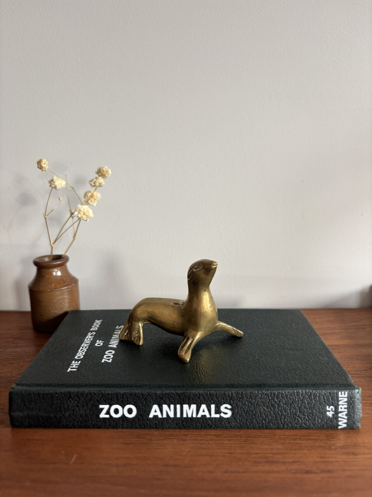 Small Brass Seal figurine sat on top of a black Zoo Animals book