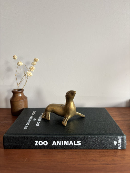 Small Brass Seal figurine sat on top of a black Zoo Animals book