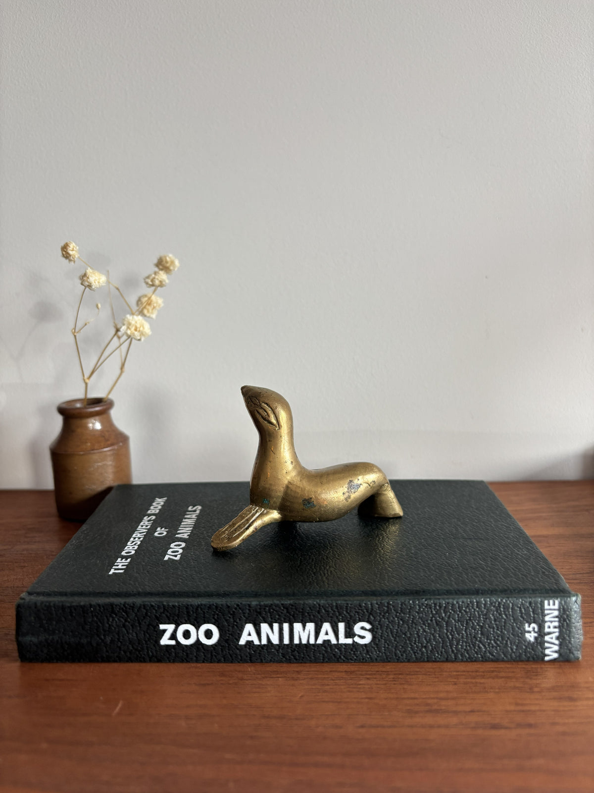 Small Brass Seal figurine sat on top of a black Zoo Animals book