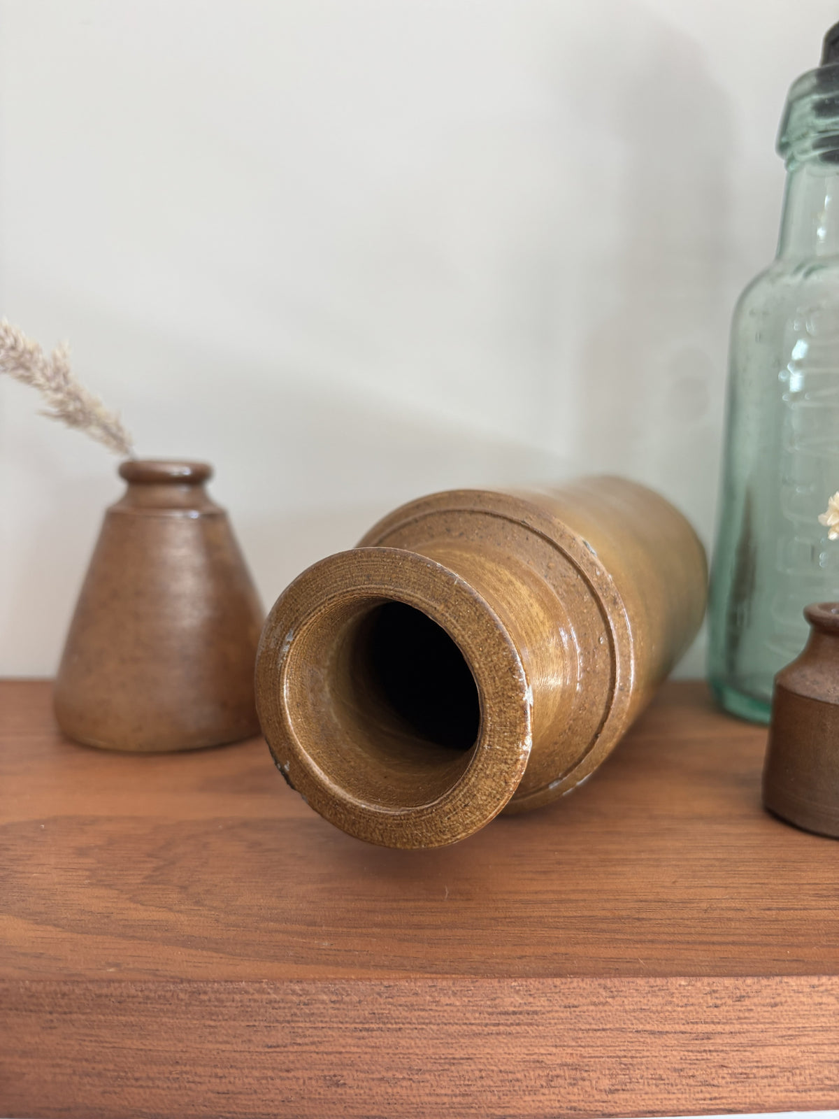 The top of a vintage brown salt glazed ink pot lying on a wooden tabletop against a plain light wall, with other decorative objects partially visible in the background.