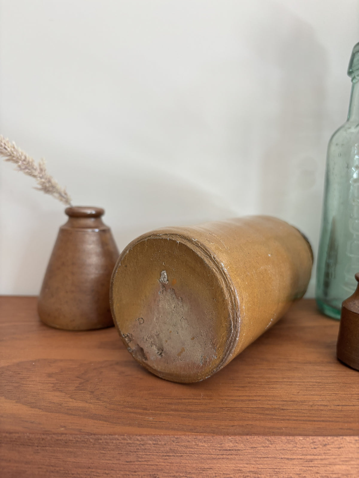 The bottom of a vintage ink pot lying on its side on a wooden tabletop next to other vintage decorative objects.