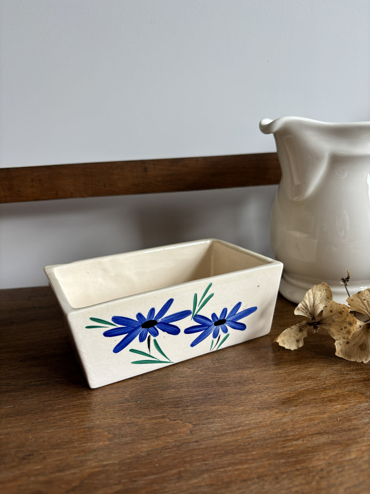 An off white ceramic vintage butter dish with a blue hand painted flower design