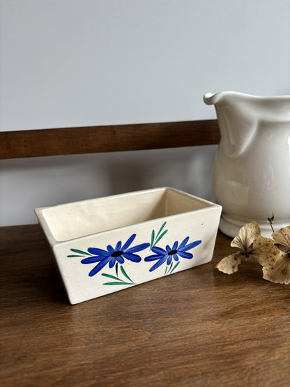 An off white ceramic vintage butter dish with a blue hand painted flower design