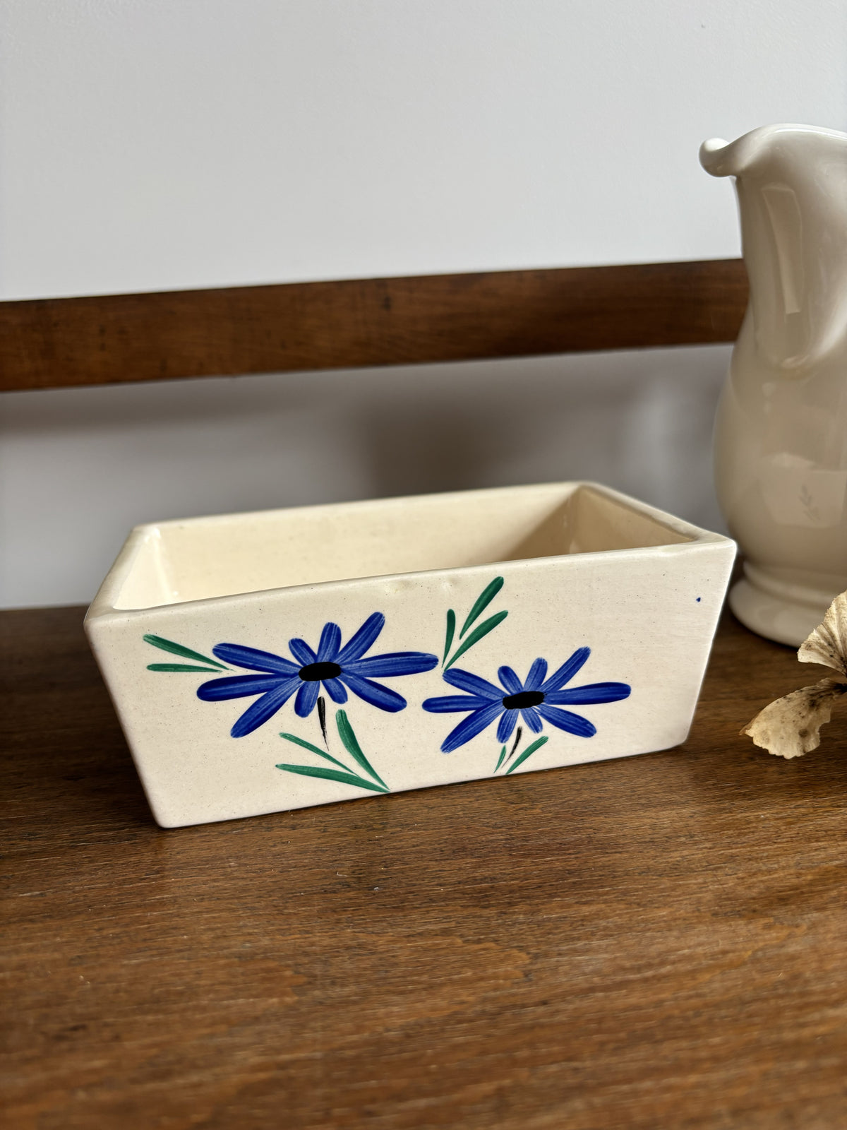 An off white ceramic vintage butter dish with a blue hand painted flower design