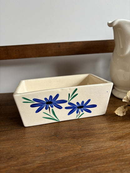 An off white ceramic vintage butter dish with a blue hand painted flower design