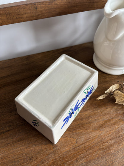 The base of an off white ceramic vintage butter dish with a blue hand painted flower design