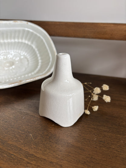A small white ceramic pie funnel standing on a dark wooden surface next to dried flowers and a matching white ceramic dish in the background.