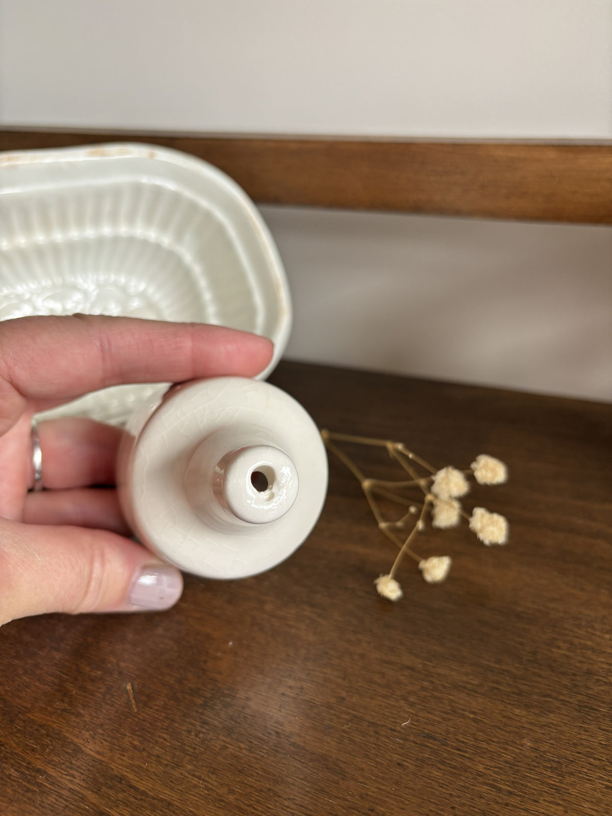 A hand holds a white ceramic pie funnel on a dark wooden surface, with a matching white ceramic tray partially visible in the background.
