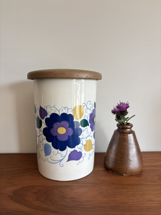 A white Crown Devon ceramic storage jar with a wooden lid, decorated with a blue, purple, and yellow floral pattern.