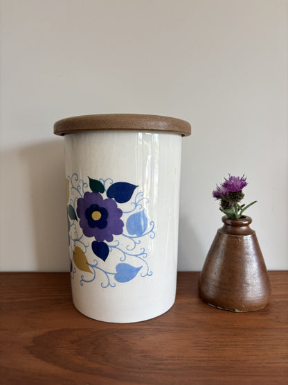 A white Crown Devon ceramic storage jar with a wooden lid, decorated with a blue, purple, and yellow floral pattern.