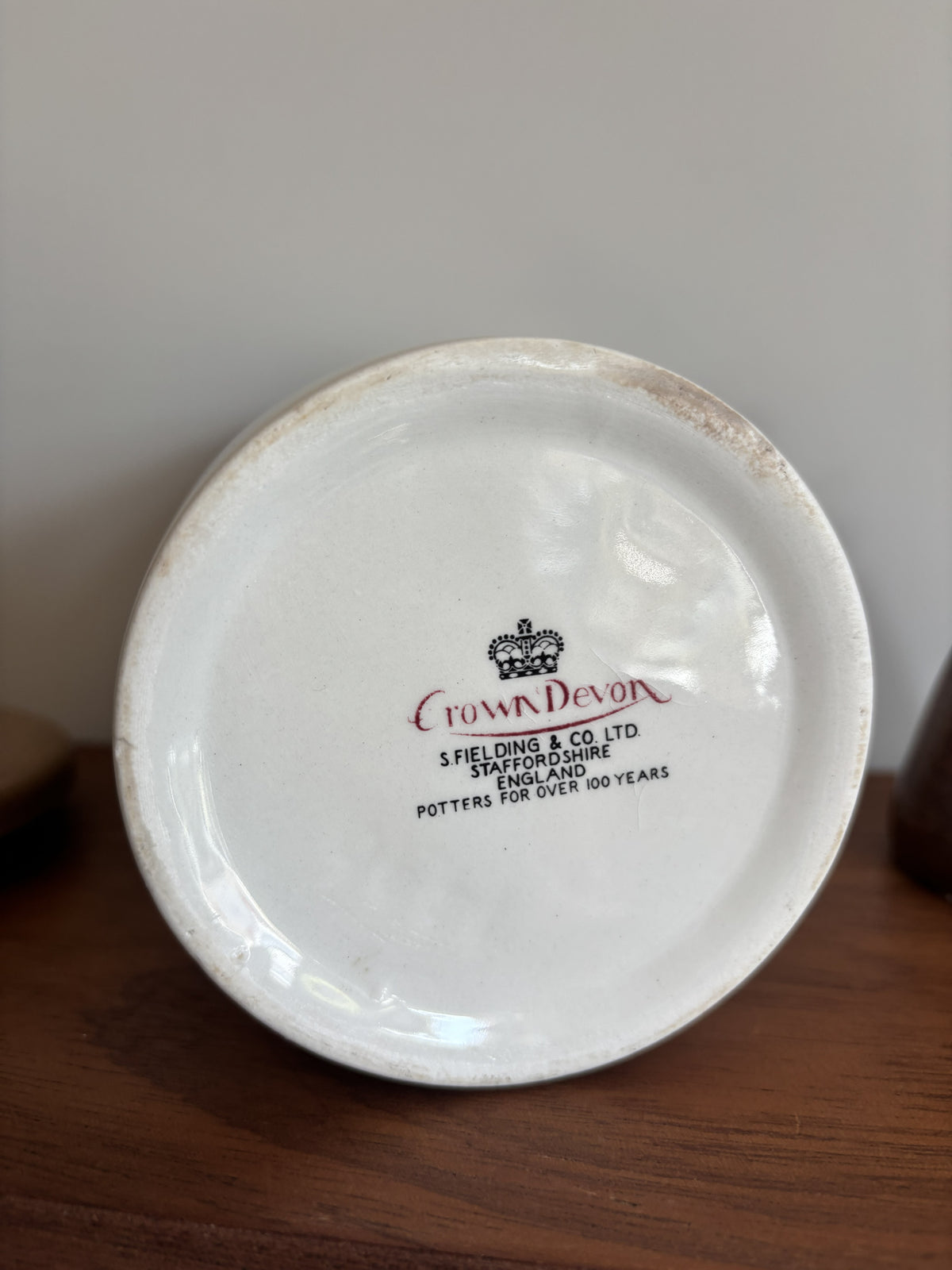 The bottom of a white Crown Devon ceramic storage jar featuring the makers mark of Crown Devon.  
