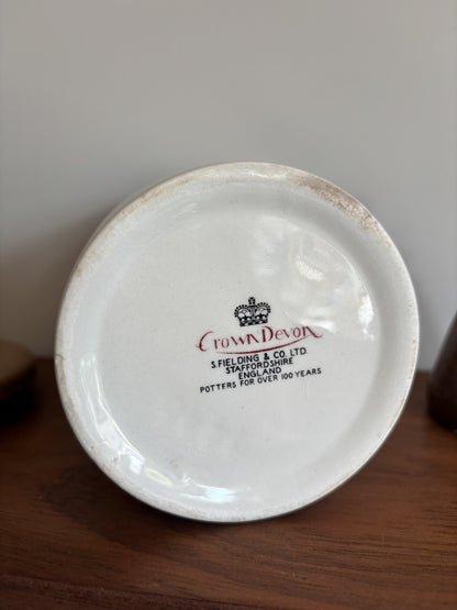 The bottom of a white Crown Devon ceramic storage jar featuring the makers mark of Crown Devon.  
