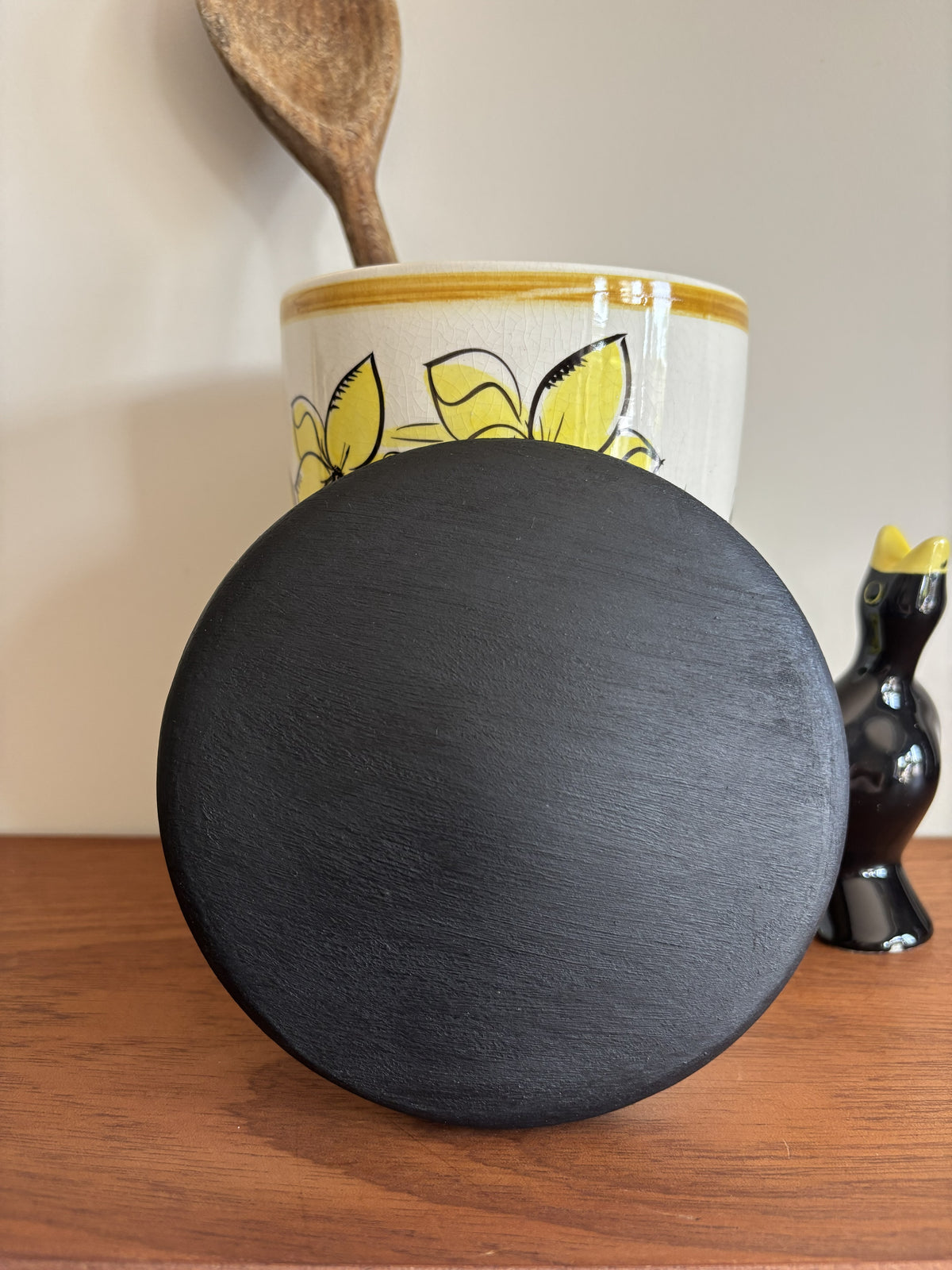 The top of a black wooden lid for a Toni Raymond storage jar. 