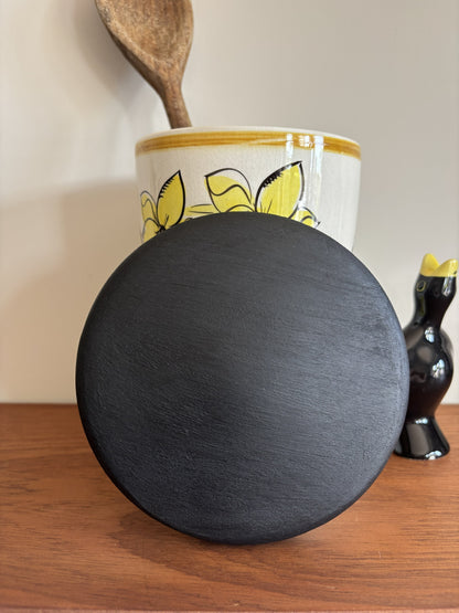 The top of a black wooden lid for a Toni Raymond storage jar. 