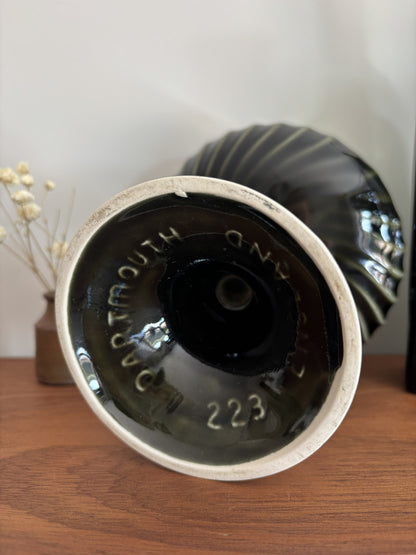 A close-up of the interior base of a dark glazed ceramic vase or planter, showing the inscription 'Dartmouth England 223' resting on a wooden surface.