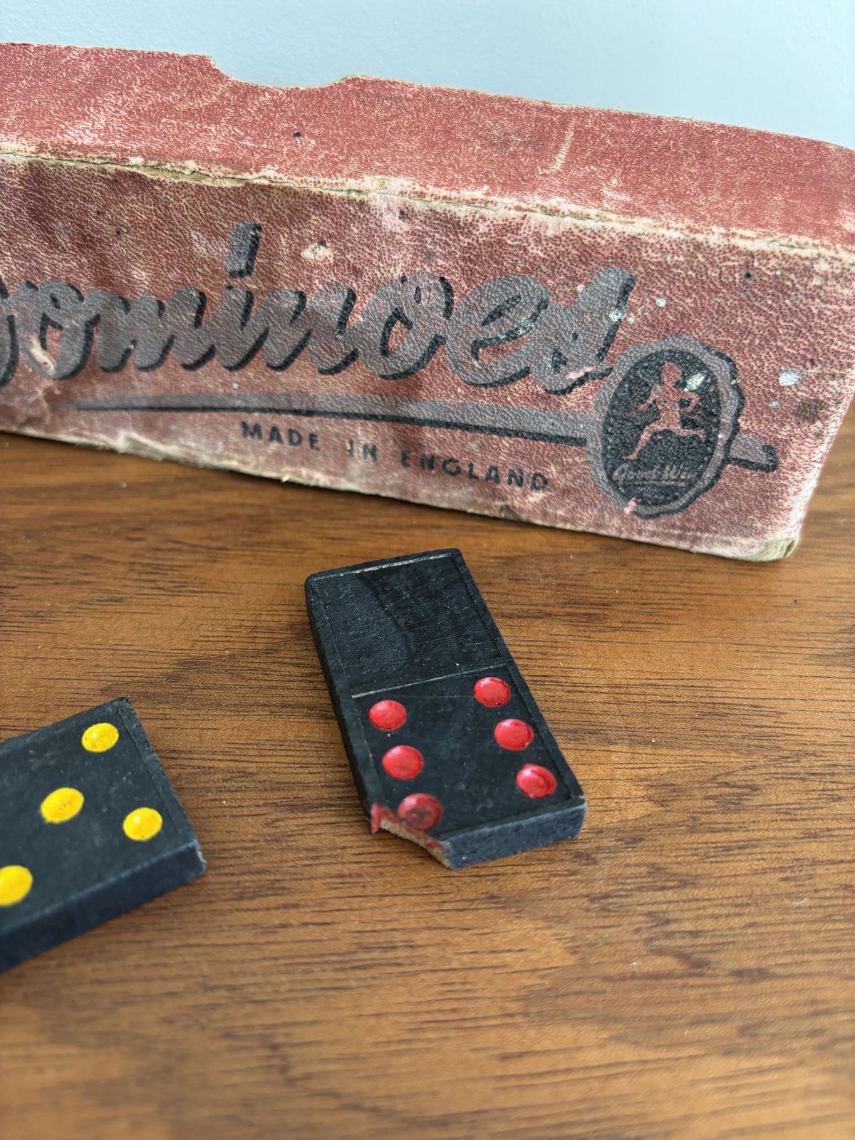 A vintage wooden domino set shown on a wooden tabletop next to two black dominoes with red and yellow pips.