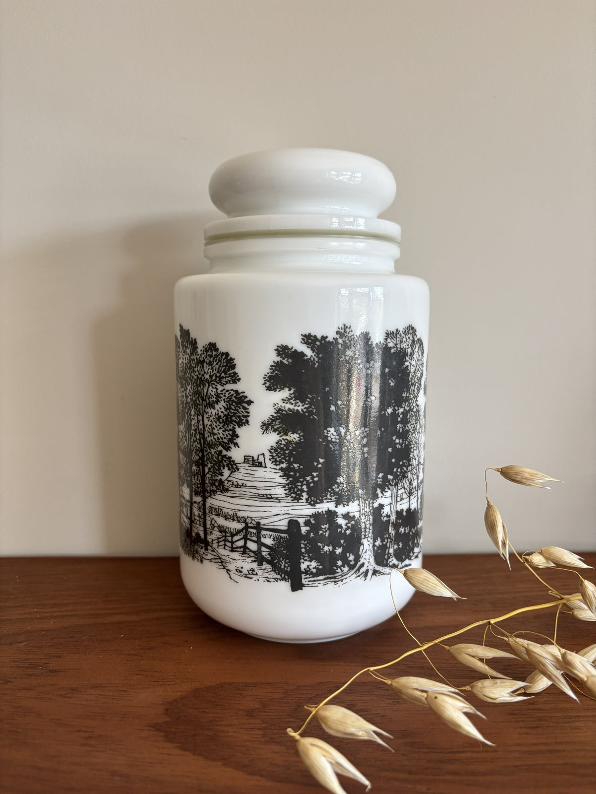 A opaline milk glass storage jar with a black transferware countryside scene.  