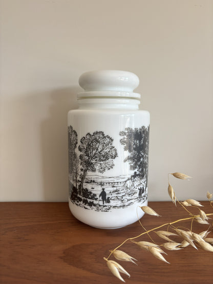 A opaline milk glass storage jar with a black transferware countryside scene.  