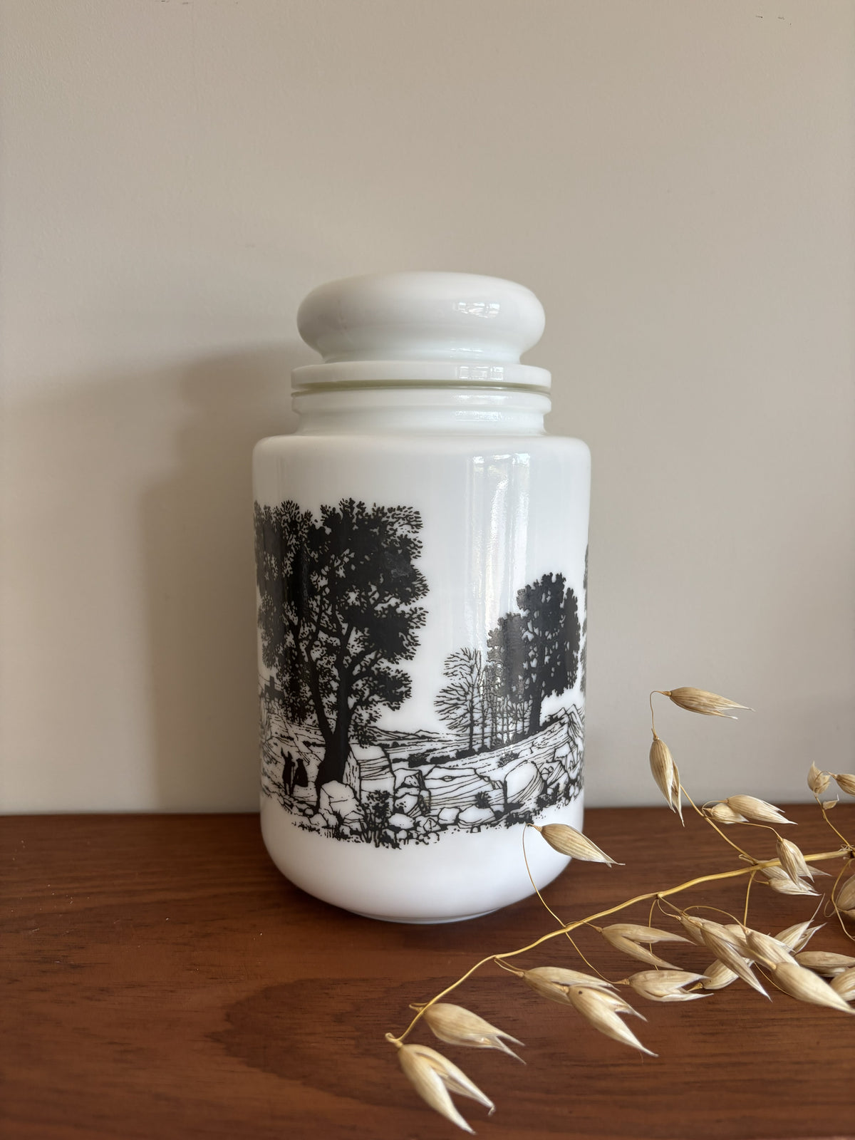 A opaline milk glass storage jar with a black transferware countryside scene.  