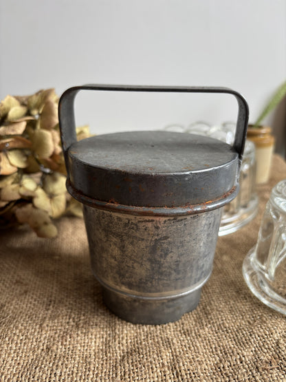 Vintage tin container with handle on a textured surface