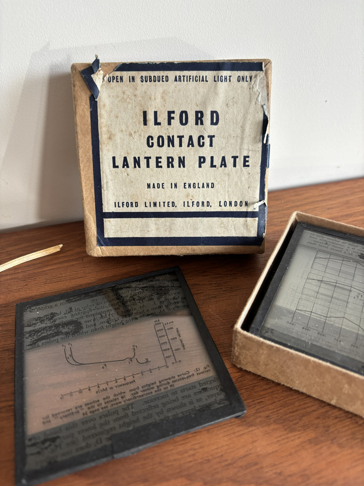 Vintage Ilford Contact Lantern Plate shown with its cardboard box and two sample plates on a wooden tabletop against a white wall.