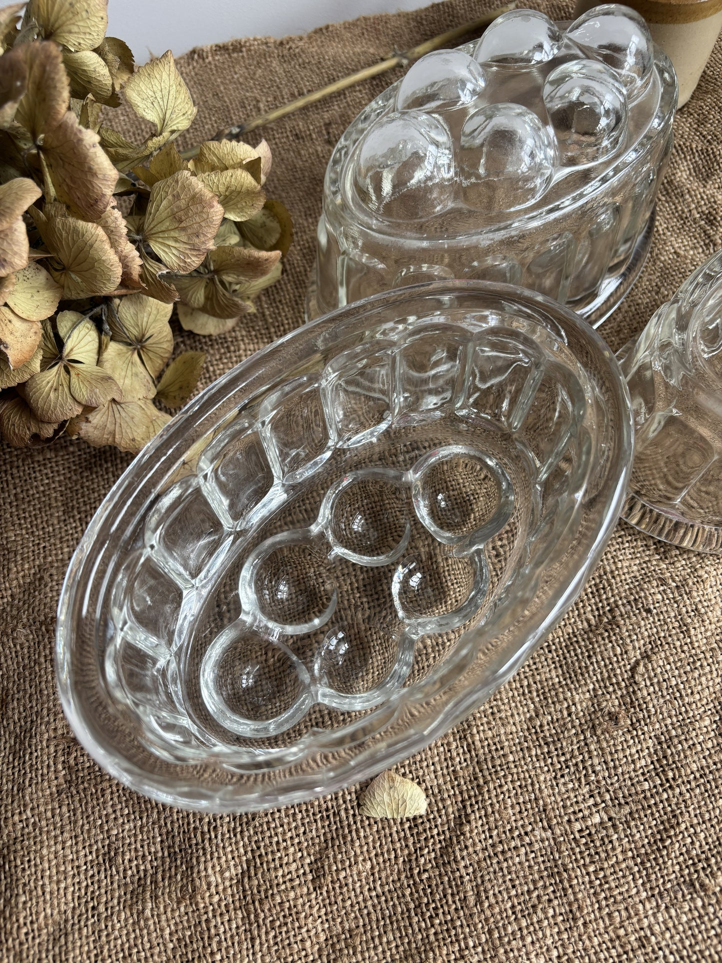 Clear glass jelly mould with embossed design on a textured surface with dried flowers.
