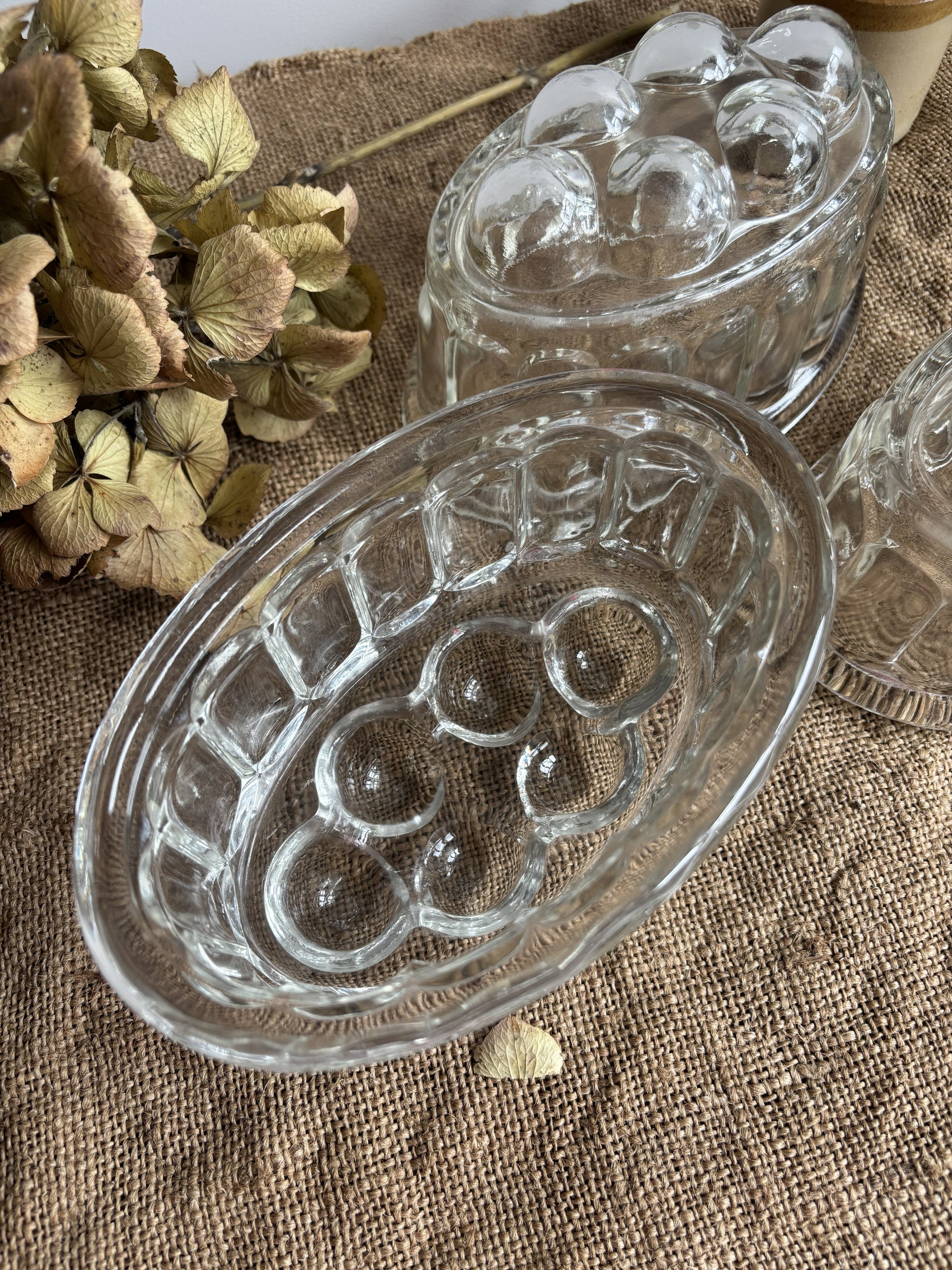 Clear glass jelly mould with embossed design on a textured surface with dried flowers.