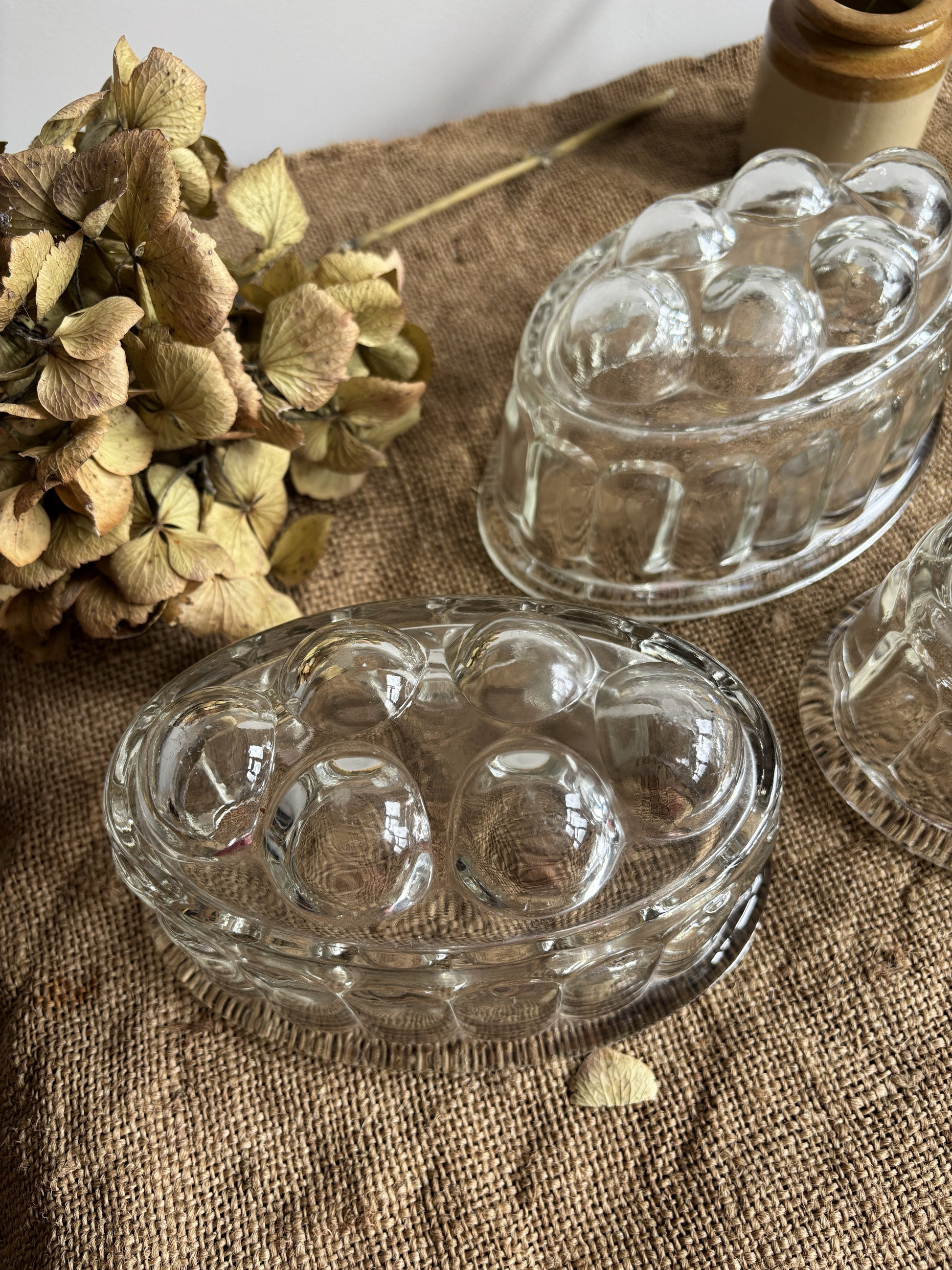Clear glass jelly mould on a textured fabric surface with dried flowers.