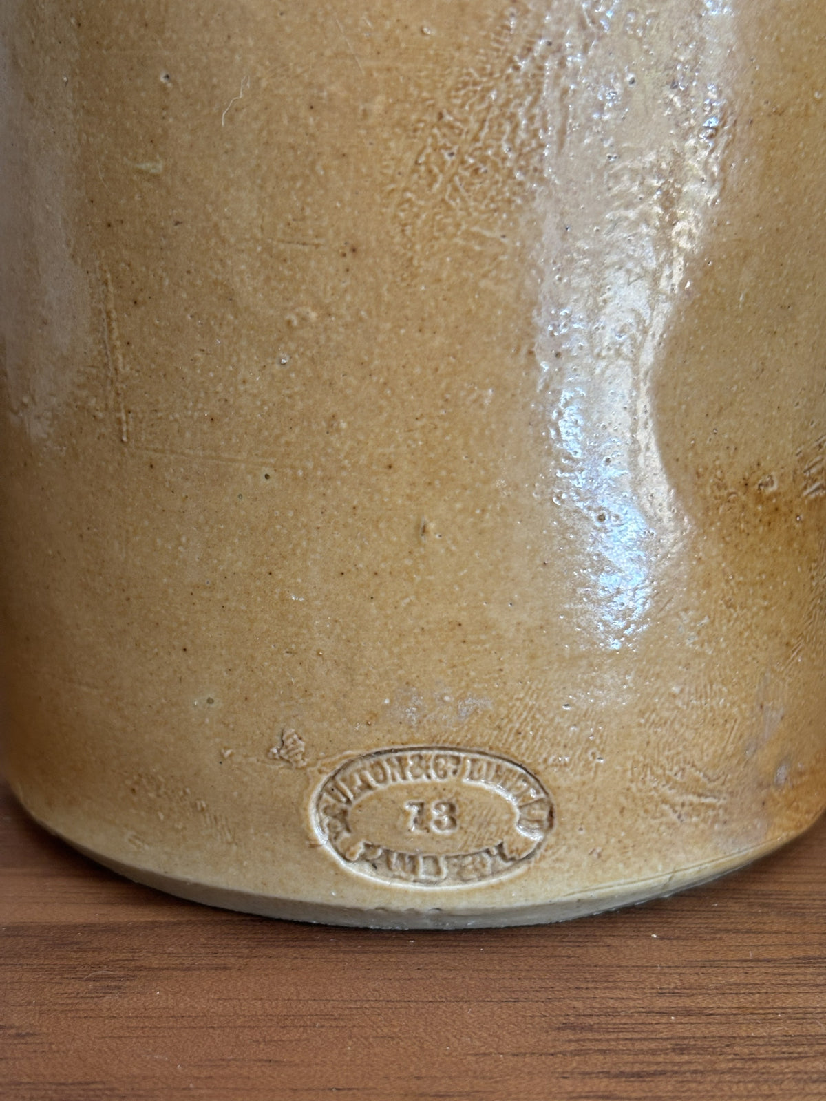 Close-up of the base of a vintage stoneware bottle, showing a glossy tan-brown glaze and an embossed circular stamp reading 'Doulton & Co Limited Lambeth' and the number '23'.