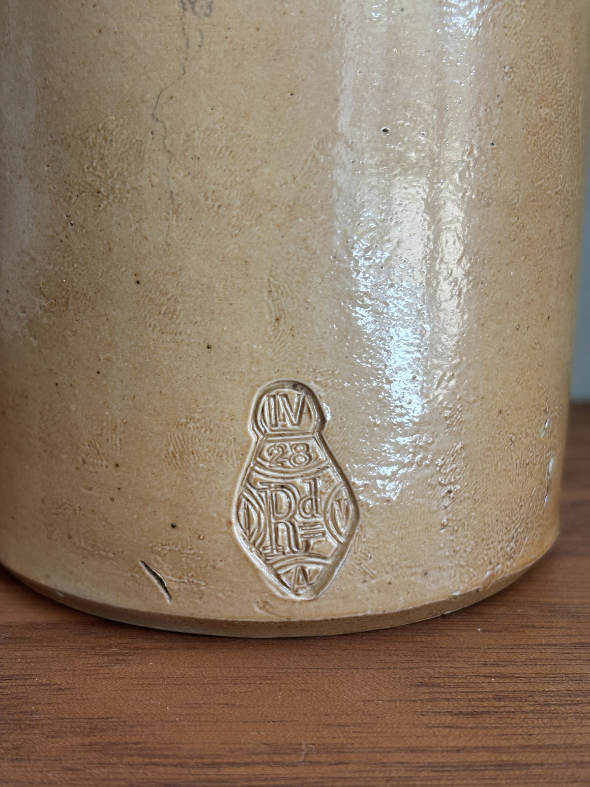 Close-up of the base of a stoneware bottle showing a glazed beige surface and an embossed maker's mark on a wooden surface.