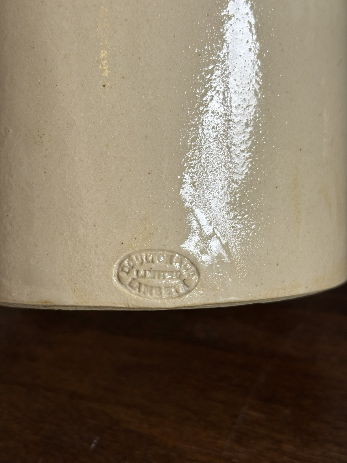 Close-up of the base of a cream-colored ceramic stoneware pot, showing a glossy finish and an embossed oval markers mark of Doulton & Co Limited Lambeth, resting on a dark wooden surface.