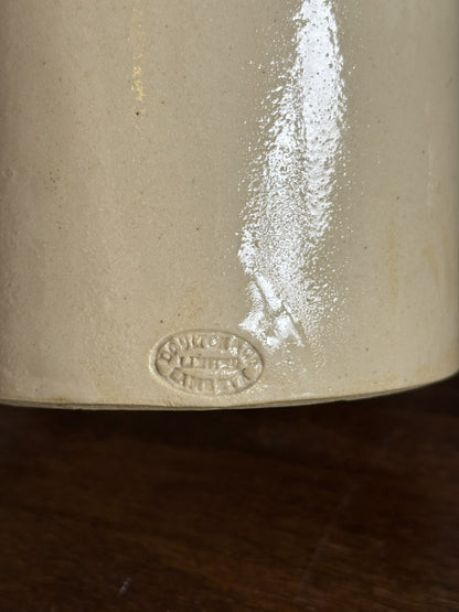 Close-up of the base of a cream-colored ceramic stoneware pot, showing a glossy finish and an embossed oval markers mark of Doulton & Co Limited Lambeth, resting on a dark wooden surface.