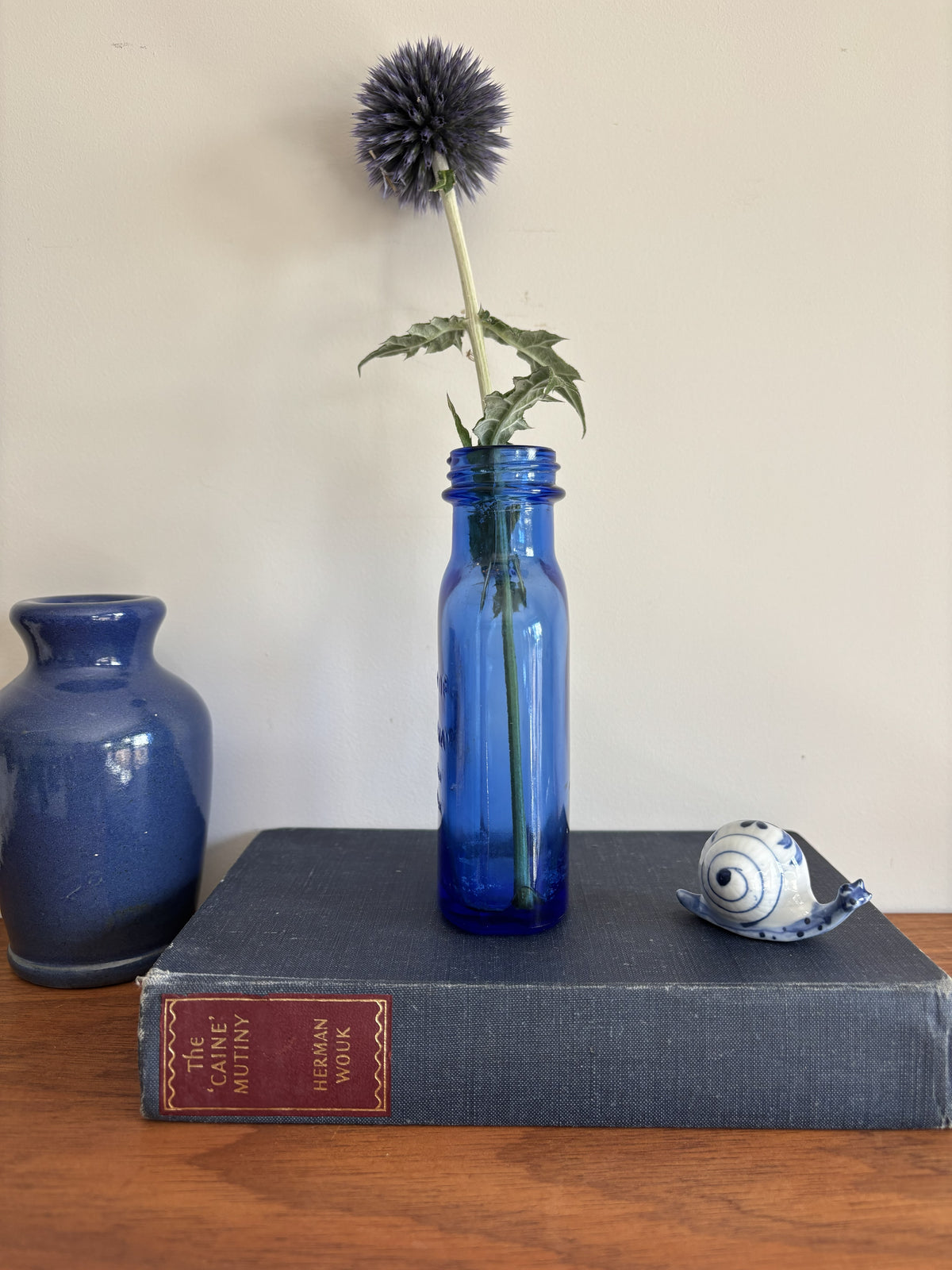 A cobalt blue vintage glass Milk of Magnesia bottle holding a single dark blue globe flower.