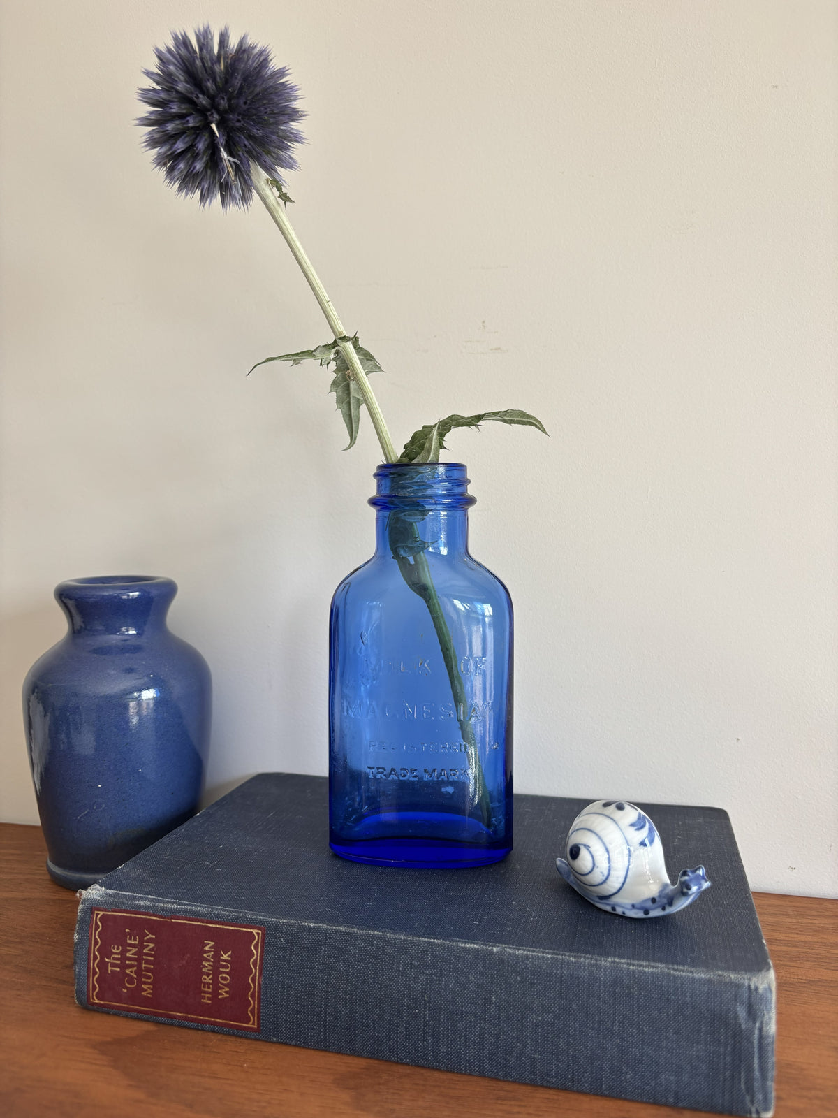 A cobalt blue vintage glass Milk of Magnesia bottle holding a single dark blue globe flower.