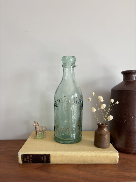A vintage aqua green Parke & White glass bottle with embossed lettering sitting on top of a yellow book.  
