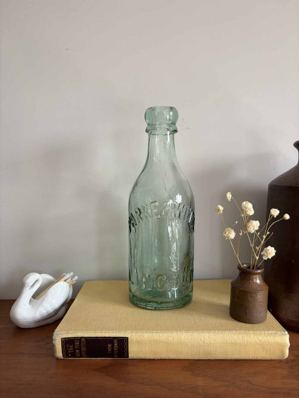 A vintage aqua green Parke & White glass bottle with embossed lettering sitting on top of a yellow book.  