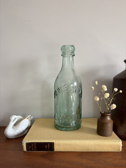A vintage aqua green Parke & White glass bottle with embossed lettering sitting on top of a yellow book.  