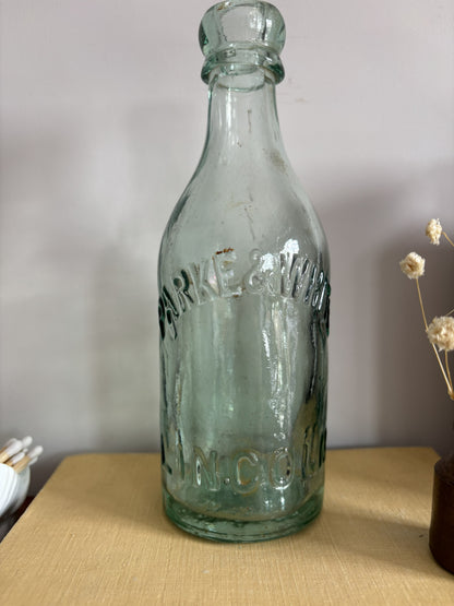 A vintage aqua green Parke & White glass bottle with embossed lettering sitting on top of a yellow book.  